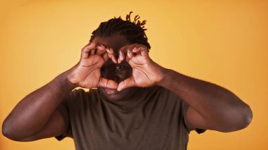 Afrikalı Amerikalı siyahi adam elleriyle kalp şekli yaratıyor ve ona bakıyor. Aşk ve ilişki kavramı