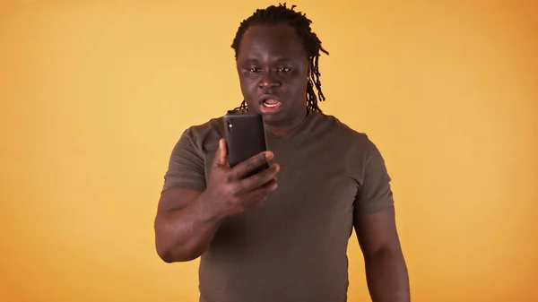 Šokovaný černoch z Afriky se dívá na obrazovku svého telefonu. Neočekávaná textová zpráva nebo špatná zpráva — Stock fotografie