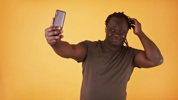 Um homem a tirar selfie. Africano americano modelo preto usando smartphone para tirar foto dele mesmo contra fundo amarelo — Fotografia de Stock