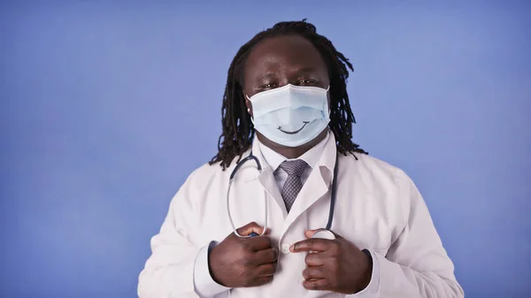 Portrait d'un médecin africain avec masque visage avec sourire sur fond bleu studio isolé — Photo