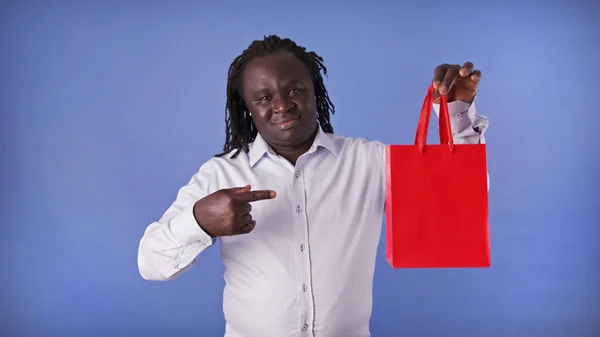 Genç Afrikalı Amerikalı siyahi adam kırmızı alışveriş torbasını işaret ediyor. Hediyeye bak. — Stok fotoğraf