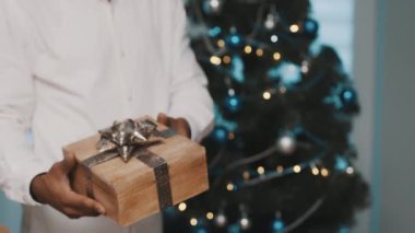 Afrikalı Amerikalı siyahi adam Noel ağacının önünde Noel hediyesi veriyor.