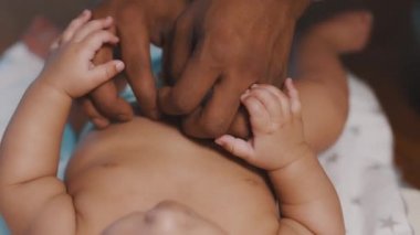 İlgilenen genç siyah baba yeni doğmuş bebeğinin karnını gıdıklıyor. Babalık ve çok ırklı aile