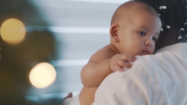 Gyönyörű újszülött mulatt baba élvezi ölelést a fekete apja közelében karácsonyfa. Nyaralás multiracionális családban — Stock videók