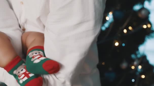 Bebê com meias de tema de Natal e papai de pé na frente da árvore de Natal. Conceito de família multirracial — Vídeo de Stock