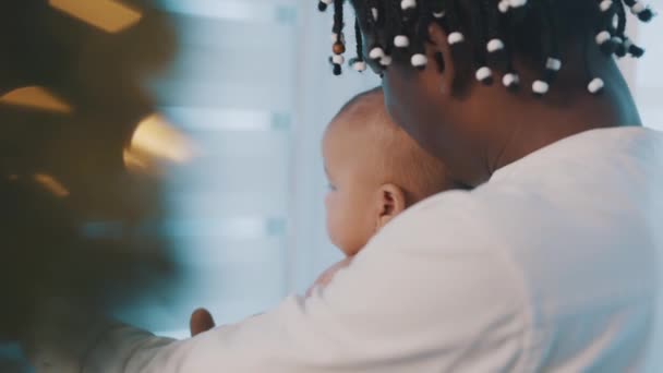 Догляд за афроамериканським батьком надувається зі своєю новонародженою дитиною біля ялинки — стокове відео