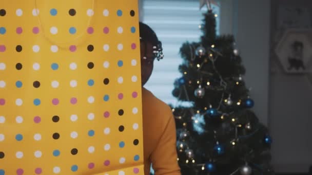 Espíritu navideño. Hombre negro afroamericano sosteniendo gran bolsa de compras de oro un regalo delante del árbol de Navidad — Vídeos de Stock
