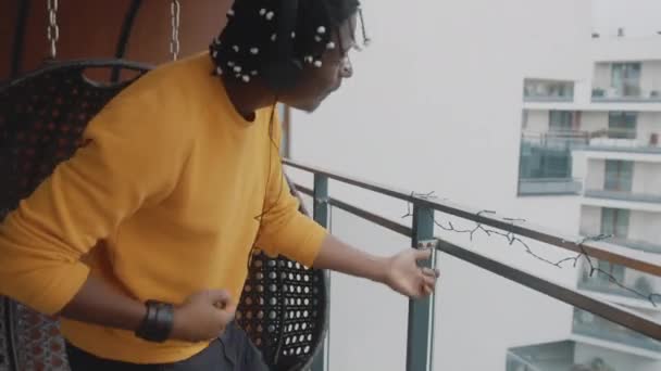 Positifity in the Lockdown. Afroamerikanischer schwarzer Mann mit Headset tanzt auf der Terrasse. — Stockvideo