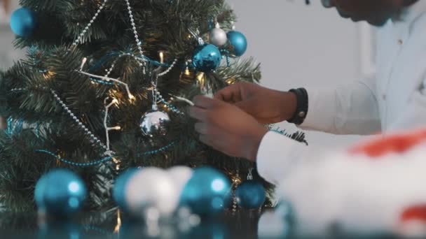 Karácsonyfa dekoráció. Közelkép a fekete ember kezét díszítő karácsonyfa kék golyók — Stock videók