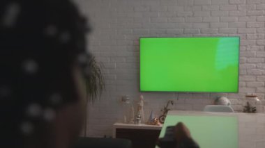 Afrikalı Amerikalı siyah adam büyük yeşil TV ekranını izliyor ve kanalları değiştiriyor.