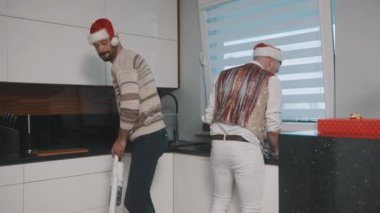 Mutlu eşcinsel çift Noel Baba şapkalarıyla mutfağı temizliyor ve eğleniyor.