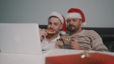 Kafkasyalı eşcinsel çift Noel arifesinde dizüstü bilgisayarda film izleyip pizza yiyorlar.
