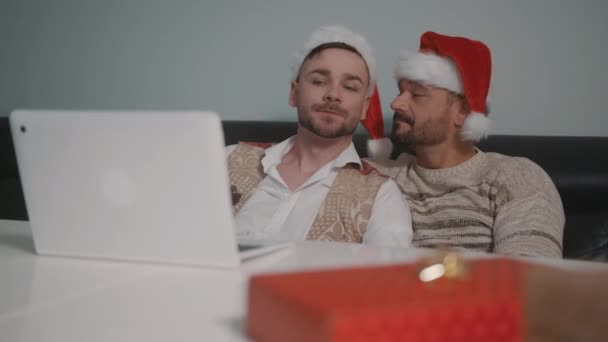 Jeune couple gay caucasien avec chapeaux Père Noël regarder des films sur l'ordinateur portable la veille de Noël — Video