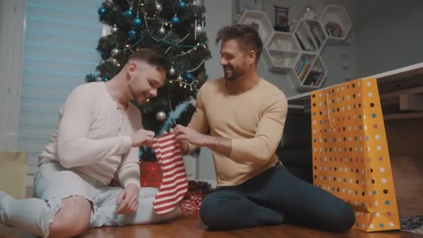 Jovem cara casal masculino presenteando uns aos outros com meias de Natal. Relacionamento homossexual e conceito de férias de inverno — Vídeo de Stock