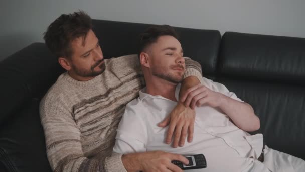 Jovem cara casal masculino abraçando no sofá e assistindo tv — Vídeo de Stock