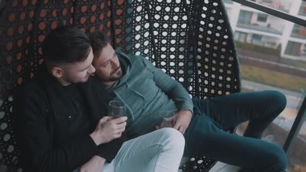 Feliz pareja homosexual relajándose y bebiendo cerveza en el balcón. Amor y afecto de parejas del mismo sexo — Vídeos de Stock