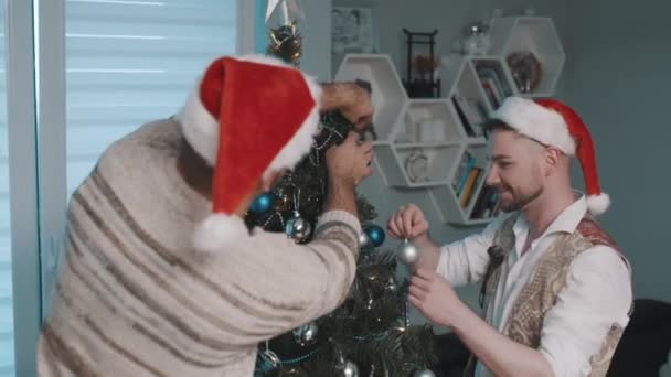 Attraktivt manligt homosexuellt par som firar nyår, dekorerar julgranen tillsammans. Lycklig familj njuter av semestern — Stockvideo