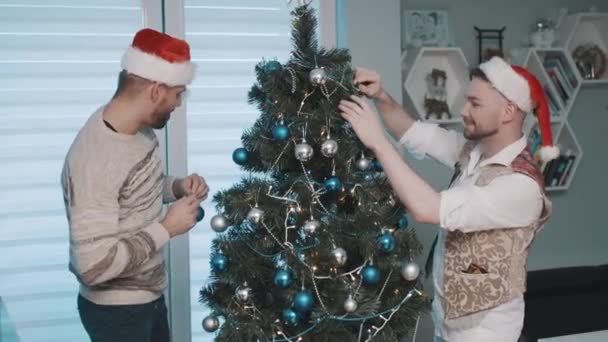 Szczęśliwy mężczyzna gej para w dom wiszące dekoracje na Boże Narodzenie drzewo razem — Wideo stockowe
