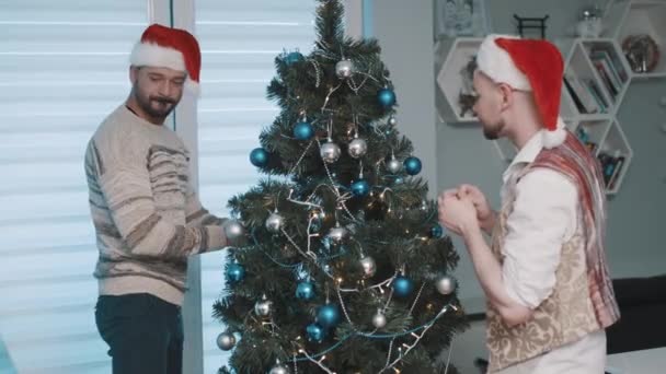 Gej mężczyzna para w dom wiszące dekoracje na Boże Narodzenie drzewo razem — Wideo stockowe