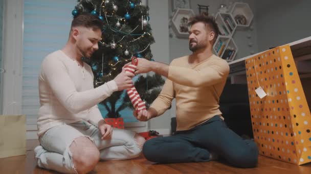 Szczęśliwa para facetów obdarowująca się świątecznymi pończochami. Pojęcie związku homoseksualnego i wakacji zimowych — Wideo stockowe
