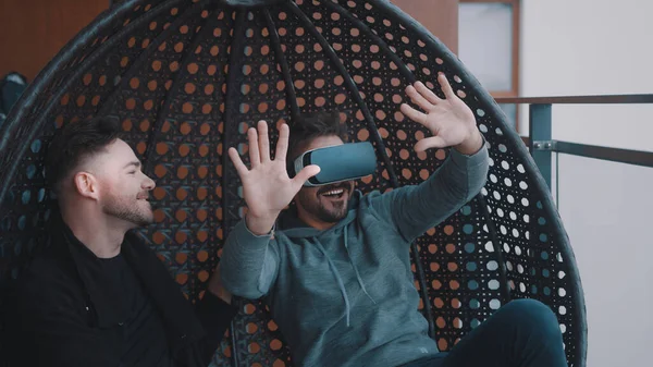 Молодой человек в защитных очках сидит на качелях со своим другом. Разработчики тестируют очки виртуальной реальности. — стоковое фото