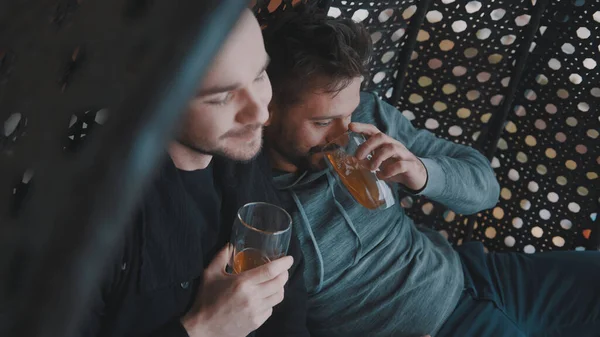 Χαρούμενο ομοφυλόφιλο ζευγάρι χαλαρώνει και πίνει μπύρα στο μπαλκόνι. Αγάπη και στοργή συντρόφων του ίδιου φύλου — Φωτογραφία Αρχείου