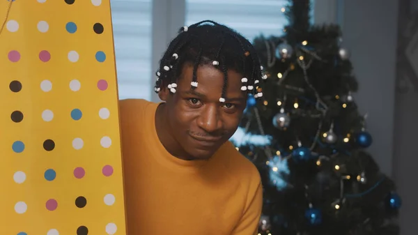 Afro-Amerikaanse zwarte man met grote gouden boodschappentas een geschenk in de voorkant van de kerstboom — Stockfoto