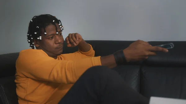 Ontspannen jonge zwarte man thuis tv kijken, het veranderen van de kanalen met behulp van afstandsbediening — Stockfoto