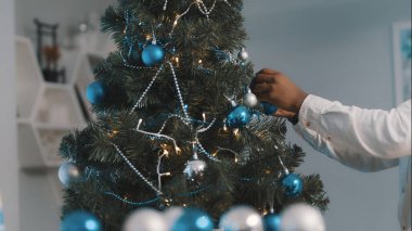 Noel ağacı süslemesi. Siyah adamın elleri, Noel ağacını mavi taşaklarla süslüyor.