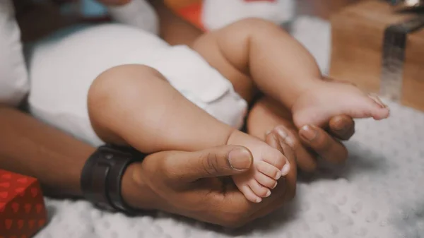 Großaufnahme, Papa hält süße Babyfüße, umgeben von Weihnachtsgeschenken — Stockfoto