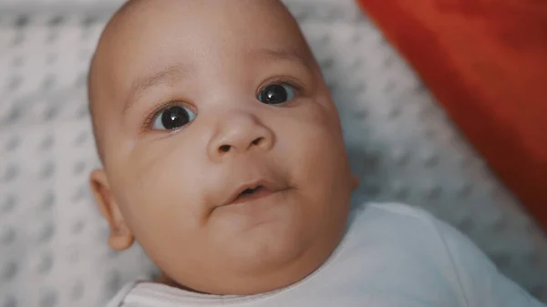 Niedliches Baby mit dunkler Haut und Weihnachtsmütze, umgeben von Geschenken, die sich auf der Decke unter dem Weihnachtsbaum entspannen — Stockfoto