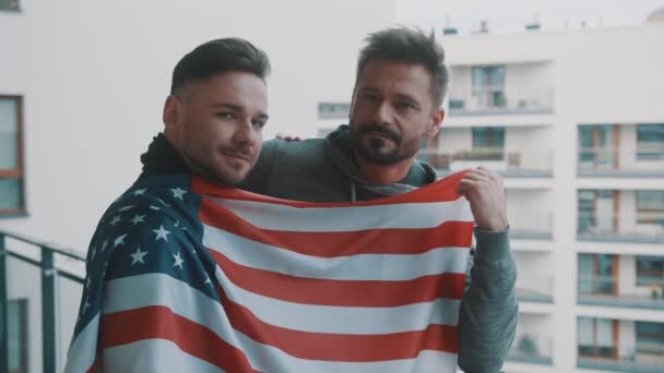 미국 국기로 덮인 발코니에서 있는 젊고 잘생긴 동성애자 부부 — 비디오