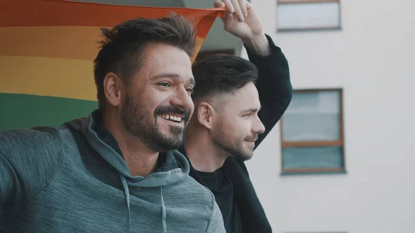 Jong opgewonden gay man paar staande op het balkon bedekt met regenboog vlag — Stockfoto