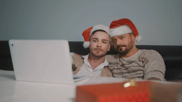 Joven pareja gay caucásica con sombreros de Santa Claus viendo películas en el portátil en la víspera de Navidad — Foto de Stock