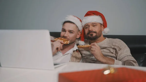 Забавная кавказская гей-пара смотрит фильмы на ноутбуке в канун Рождества и ест пиццу — стоковое фото