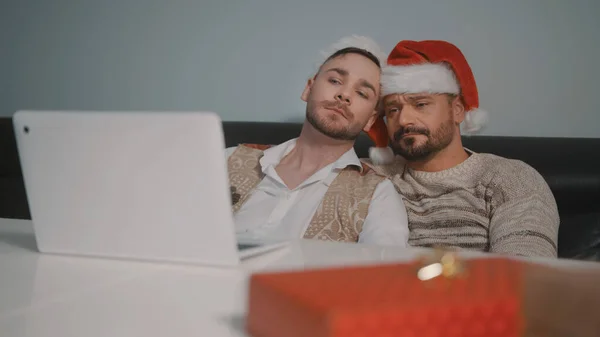 Feliz gay macho pareja con santa claus sombreros mimos y viendo película en la navidad víspera — Foto de Stock