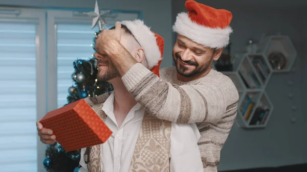 Novio sorprendiendo a su pareja masculina con regalo de Navidad. feliz gay pareja pasando Navidad víspera juntos — Foto de Stock