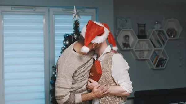 Navidad en familia gay, abrazos delante del árbol de Navidad con regalos y sombreros de Santa Claus — Foto de Stock