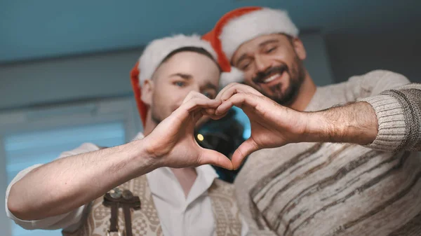 Hombres gay pareja con santa sombreros haciendo corazón forma con sus manos — Foto de Stock