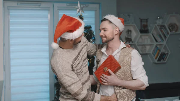 Novio sorprendiendo a su pareja masculina con regalo de Navidad. feliz gay pareja pasando Navidad víspera juntos — Foto de Stock