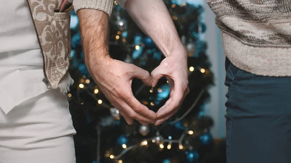 Erkek, eşcinsel, kalbi şekillendiriyor. Süslü Noel ağacının önünde elleriyle.. — Stok fotoğraf