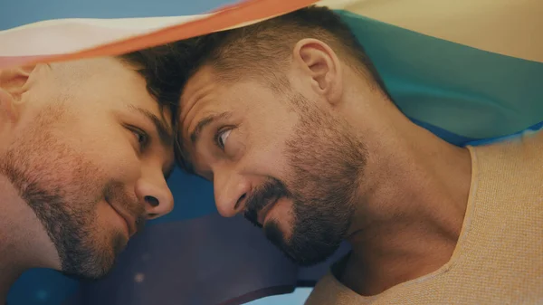 Portret van twee jonge knappe homoseksuele mannen bedekt met regenboogvlag die elkaar aankijken — Stockfoto