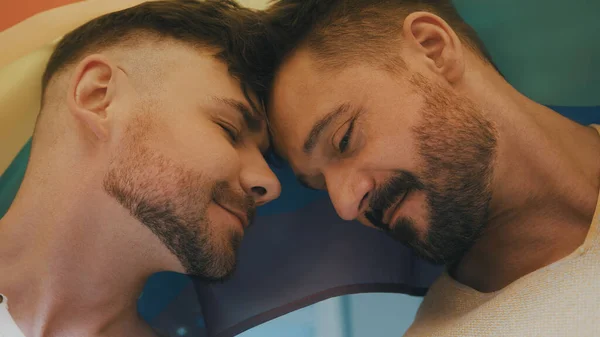 Портрет двух молодых красивых гомосексуальных мужчин, покрытых радужным флагом, смотрящих друг на друга — стоковое фото