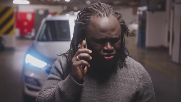 Złe wieści. Afroamerykanin czarny zestresowany mężczyzna prowadzi nieprzyjemną rozmowę telefoniczną na podziemnym parkingu — Wideo stockowe