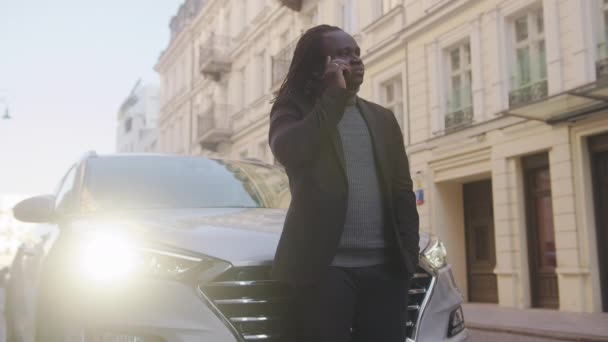 Homme d'affaires afro-américain appuyé sur la voiture, parlant au téléphone et regardant sa montre-bracelet. Le temps est argent — Video