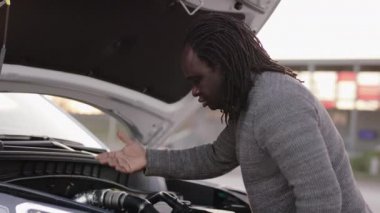 Bozuk arabayı tamir etmeye çalışan depresif Afrikalı Amerikalı siyah adam.