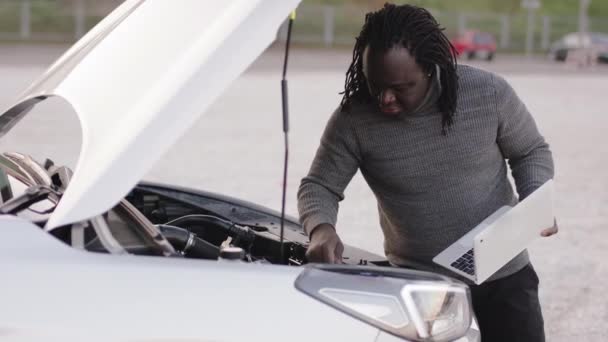 Jeune homme noir afro-américain réparer la voiture tout en utilisant un ordinateur portable — Video