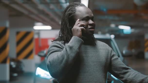 地下駐車場で話している間に電話とジェスチャーを持っている幸せなアフリカ系アメリカ人黒人男性 — ストック動画