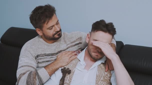 Porträt zweier gutaussehender Männer, die Beziehungsprobleme haben, wenn sie auf der Couch sitzen und sich umarmen — Stockvideo