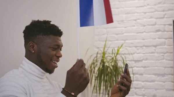 Siyah adam, Fransa bayrağı sallarken akıllı telefondan video görüşmesi yapıyor. — Stok fotoğraf